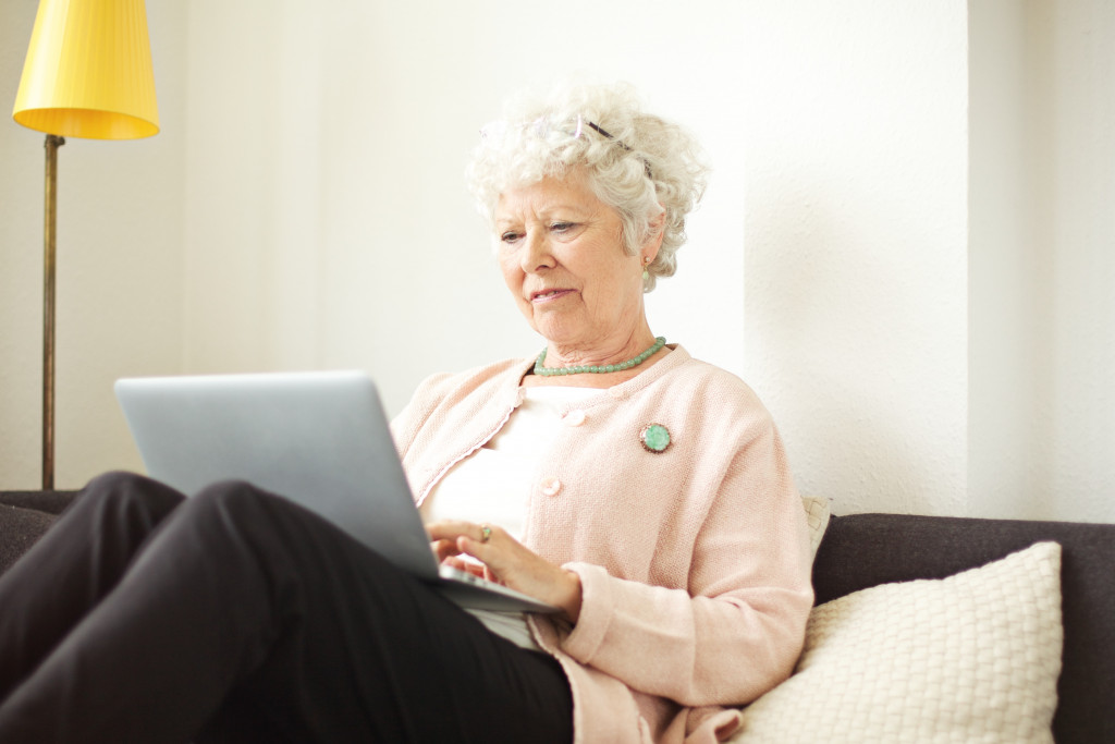 An elderly woman using a laptop on a living room couch